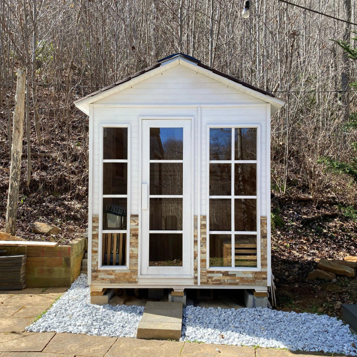 Aleko Canadian Red Cedar Stone Finish Wet/Dry Outdoor Sauna 6 Person with 6 kW Electric Sauna Heater in a yard with forest in the background.