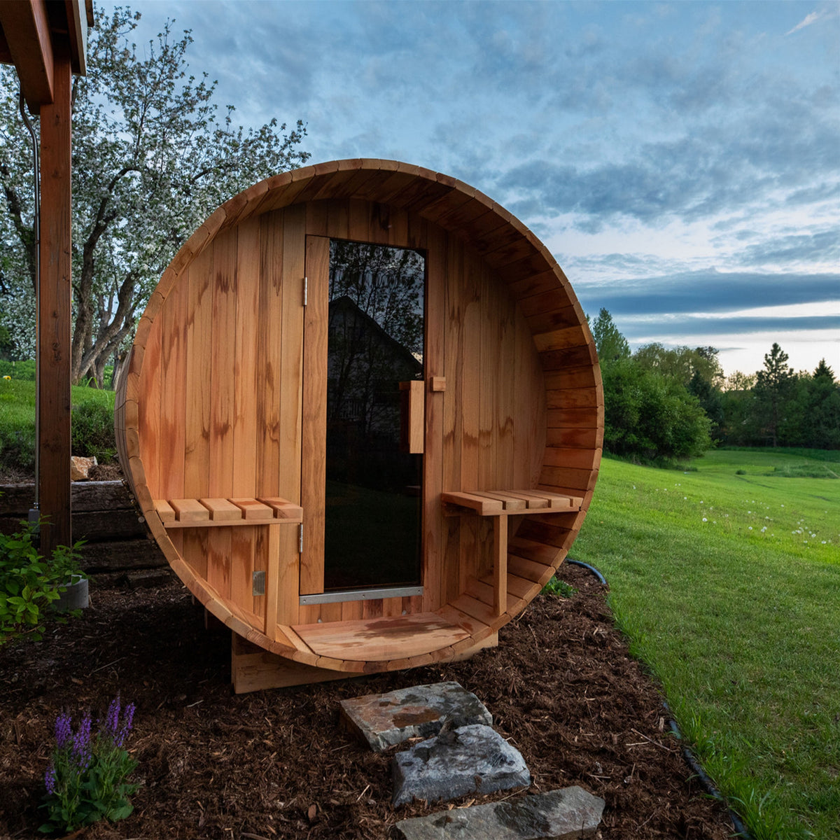 Entrance of Aleko Red Cedar Wet/Dry Outdoor Barrel Sauna with Front Porch Canopy, Panoramic View, Butimen Shingle Roofing and 8 kW KIP Harvia Electric Sauna Heater in an outdoor setting.