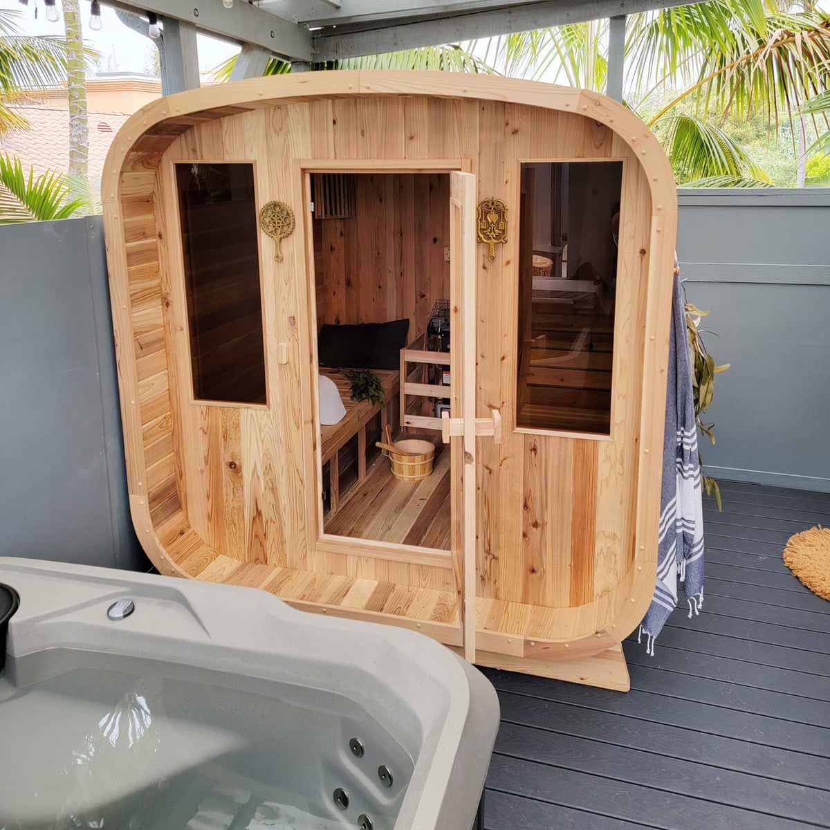 Aleko Rustic Cedar Square Outdoor Sauna 4 Person with 4.5 kW Electric Sauna Heater in a terrace.