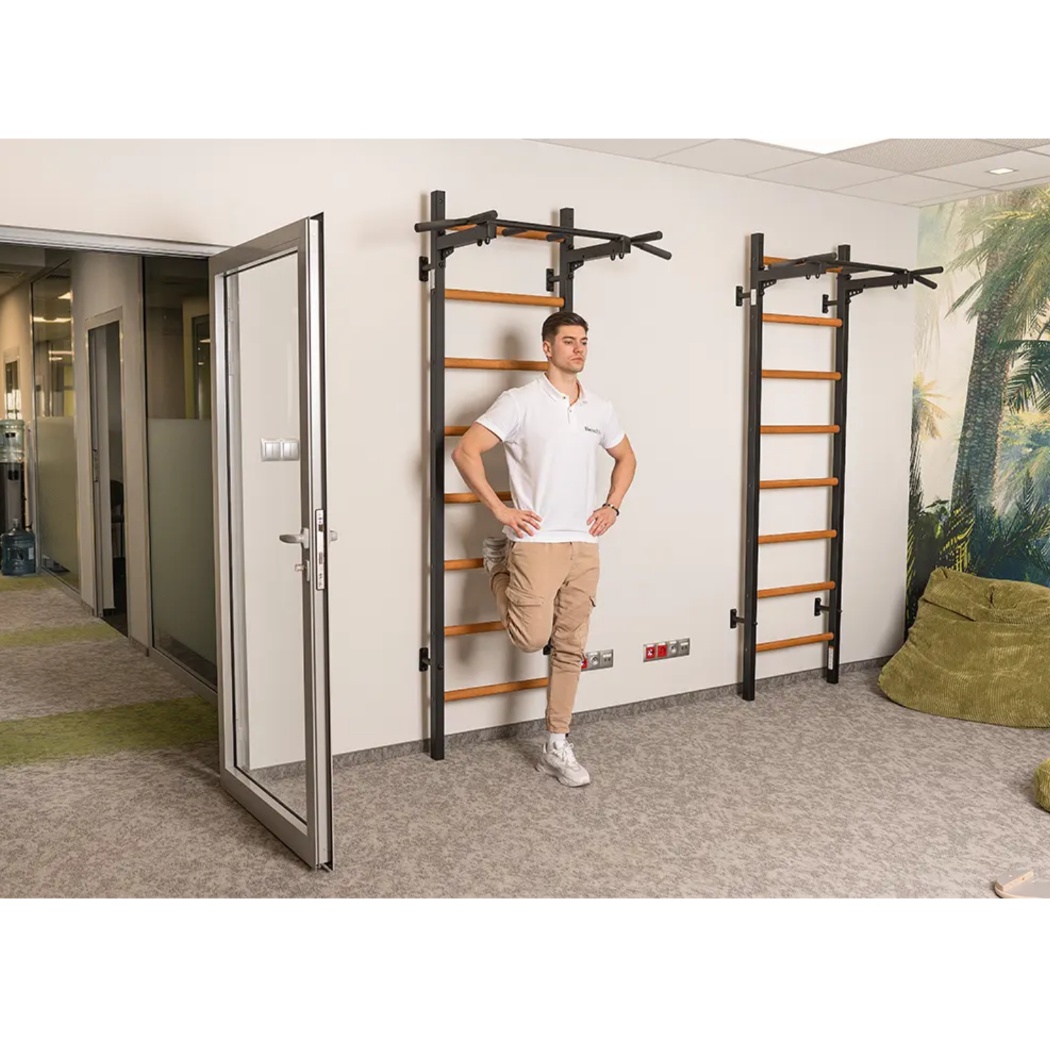 A man stretching using a BenchK 221 Wall Bars and Gymnastic Ladders black version.