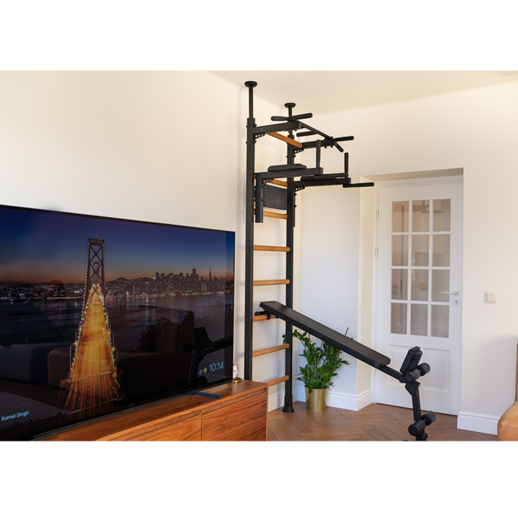 BenchK 523 Wall Bars and Gymnastic Ladders black version with pull up bar, dip bar with back rest, and workout bench installed in a living room.