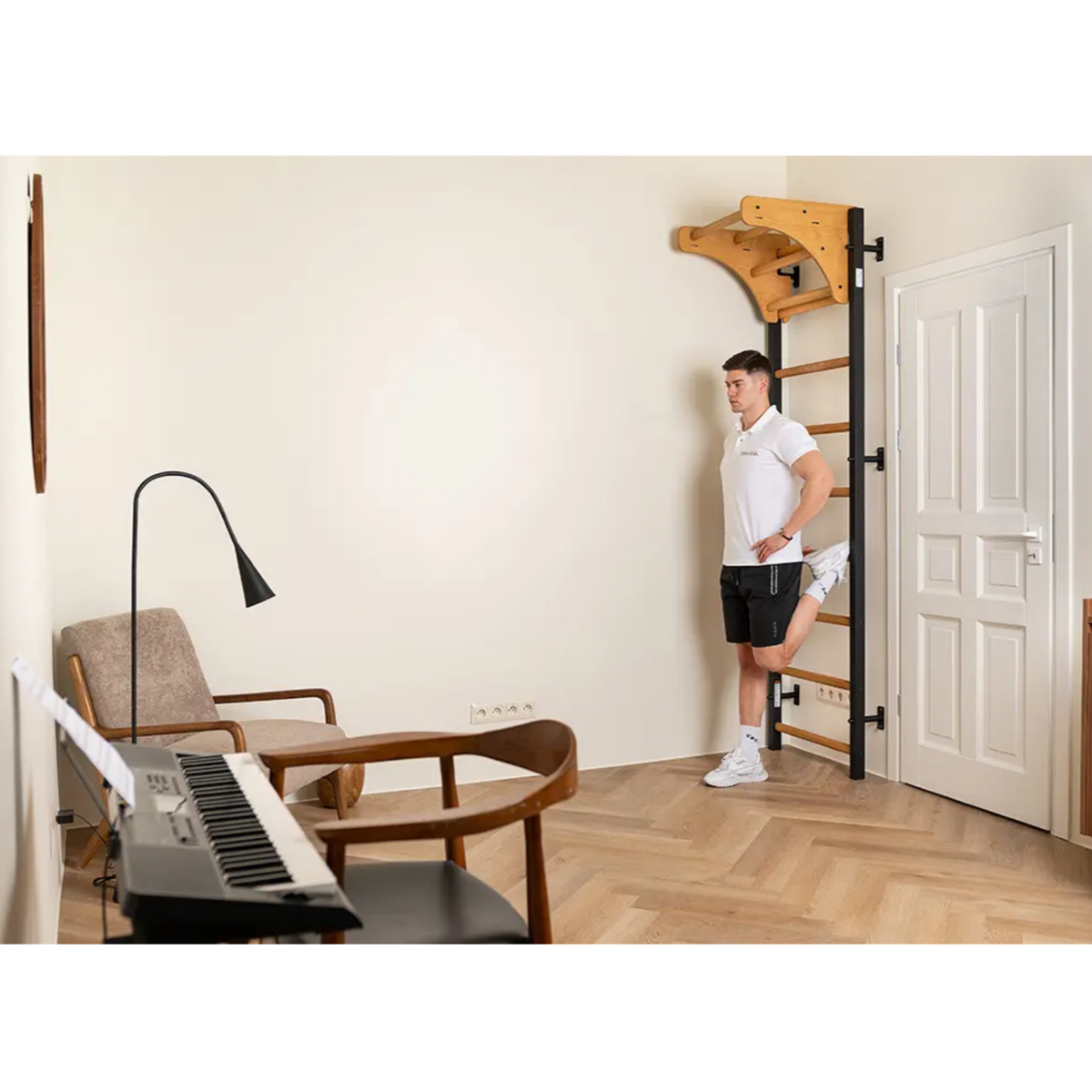 A man stretching using BenchK 711 Wall Bars and Gymnastic Ladders with wooden pull-up bar black version installed in a living room.