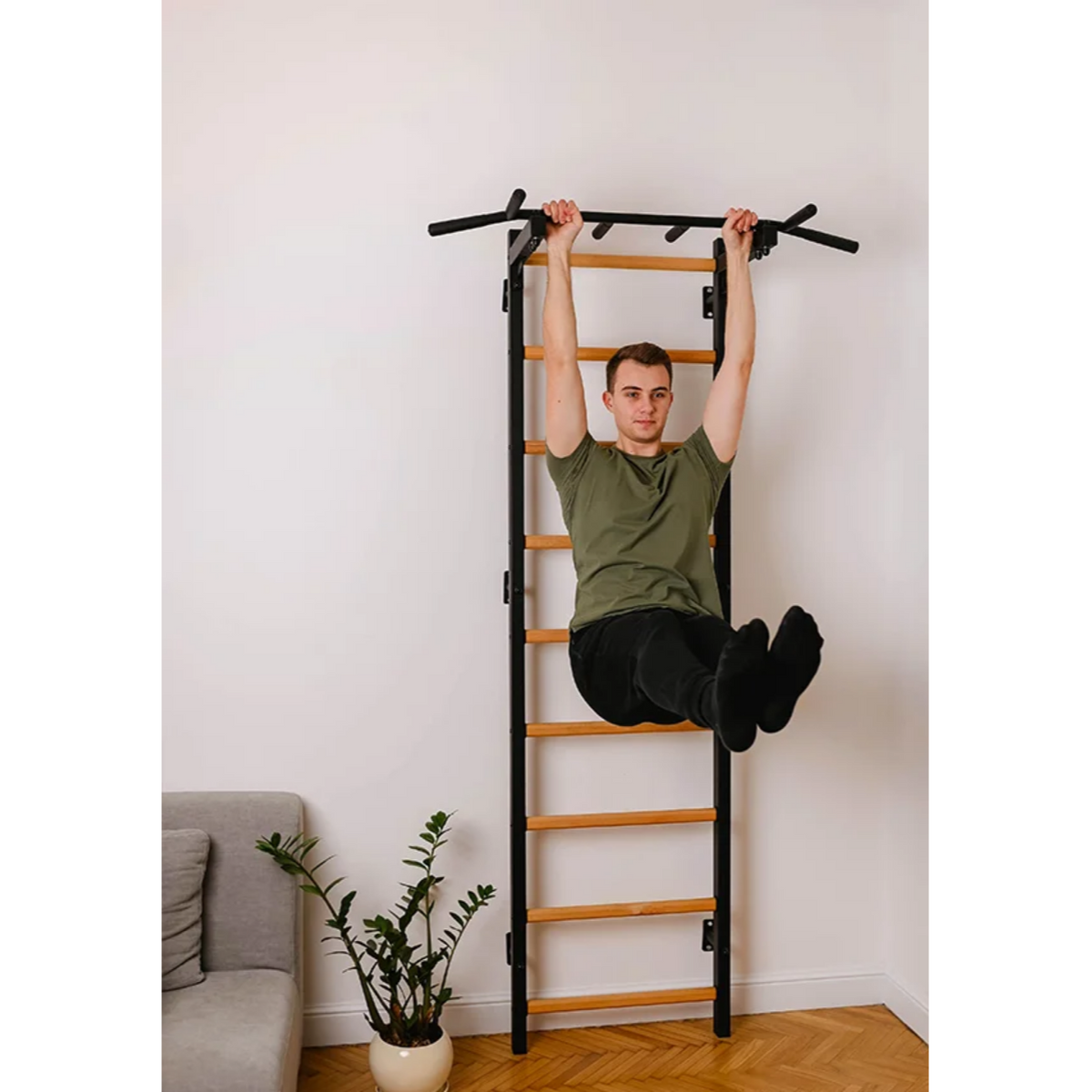 A man exercising with BenchK 721 Wall Bars + A076/A204 Gymnastic Accessories black version installed in a living room.