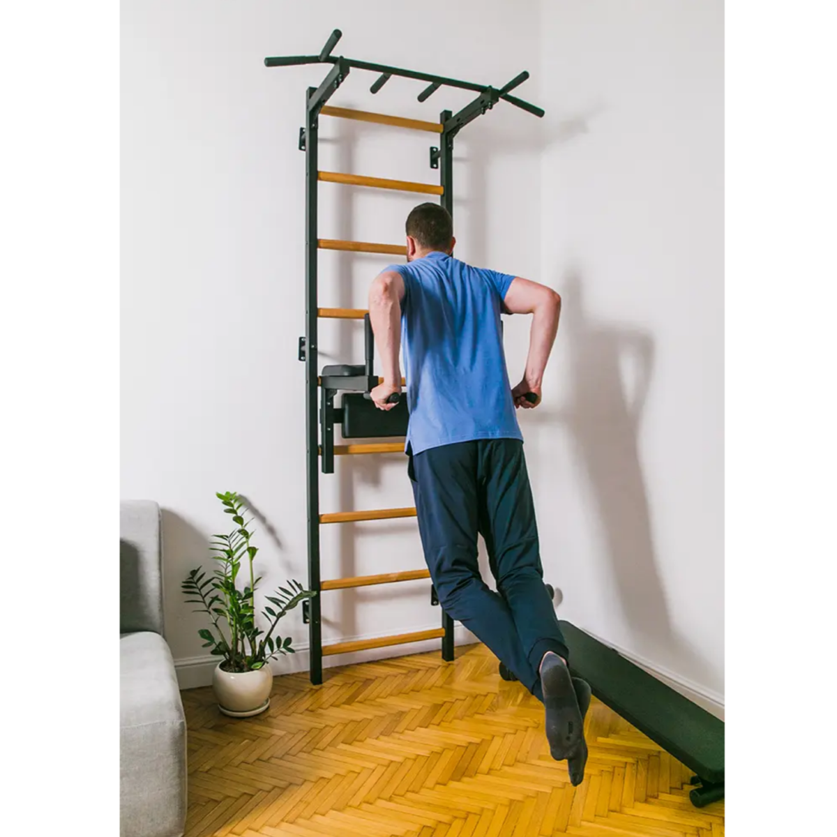 A man doing dips with BenchK 722 Wall Bars and Gymnastic Ladders black version installed in a living room.