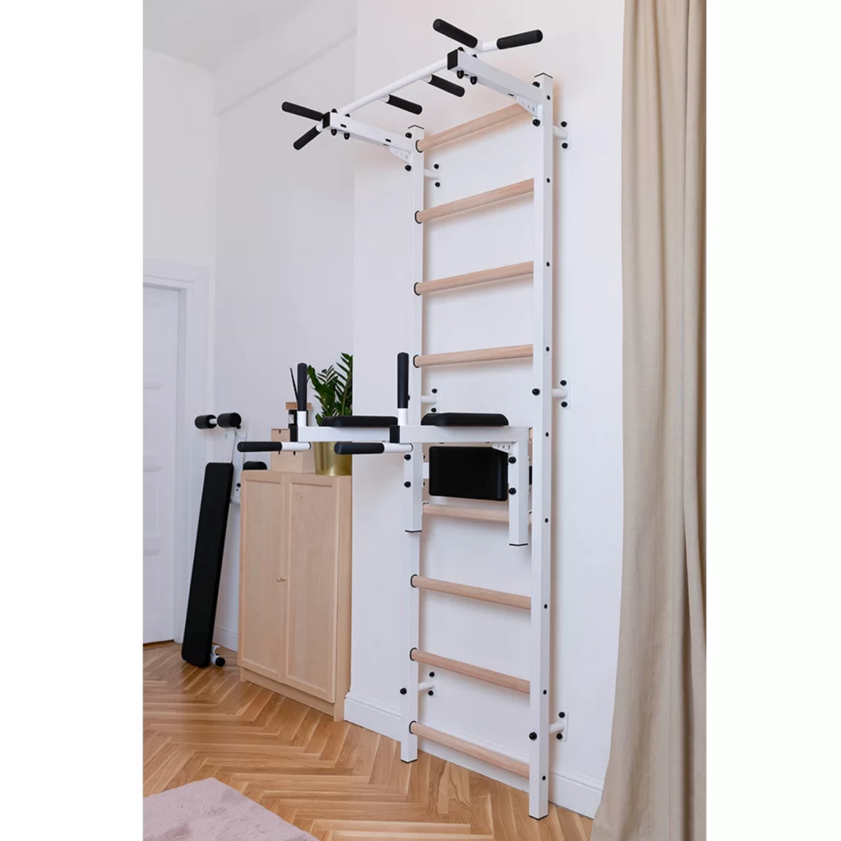 BenchK 722 Wall Bars and Gymnastic Ladders white version with pull-up bar and dip bar with back support and armrest installed in a bedroom.