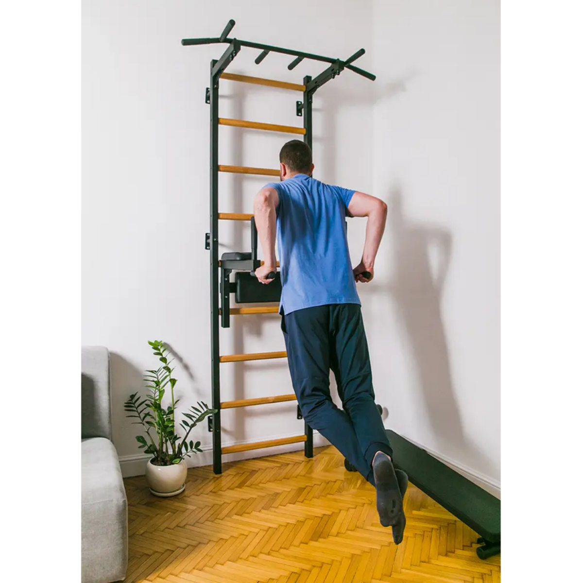 A man doing dips with BenchK 723 Wall Bars and Gymnastic Ladders black version in a living room.