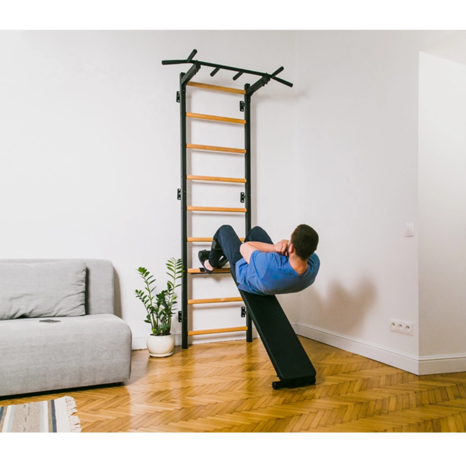 A man exercising with a BenchK 723 Wall Bars and Gymnastic Ladders black version installed in a living room.