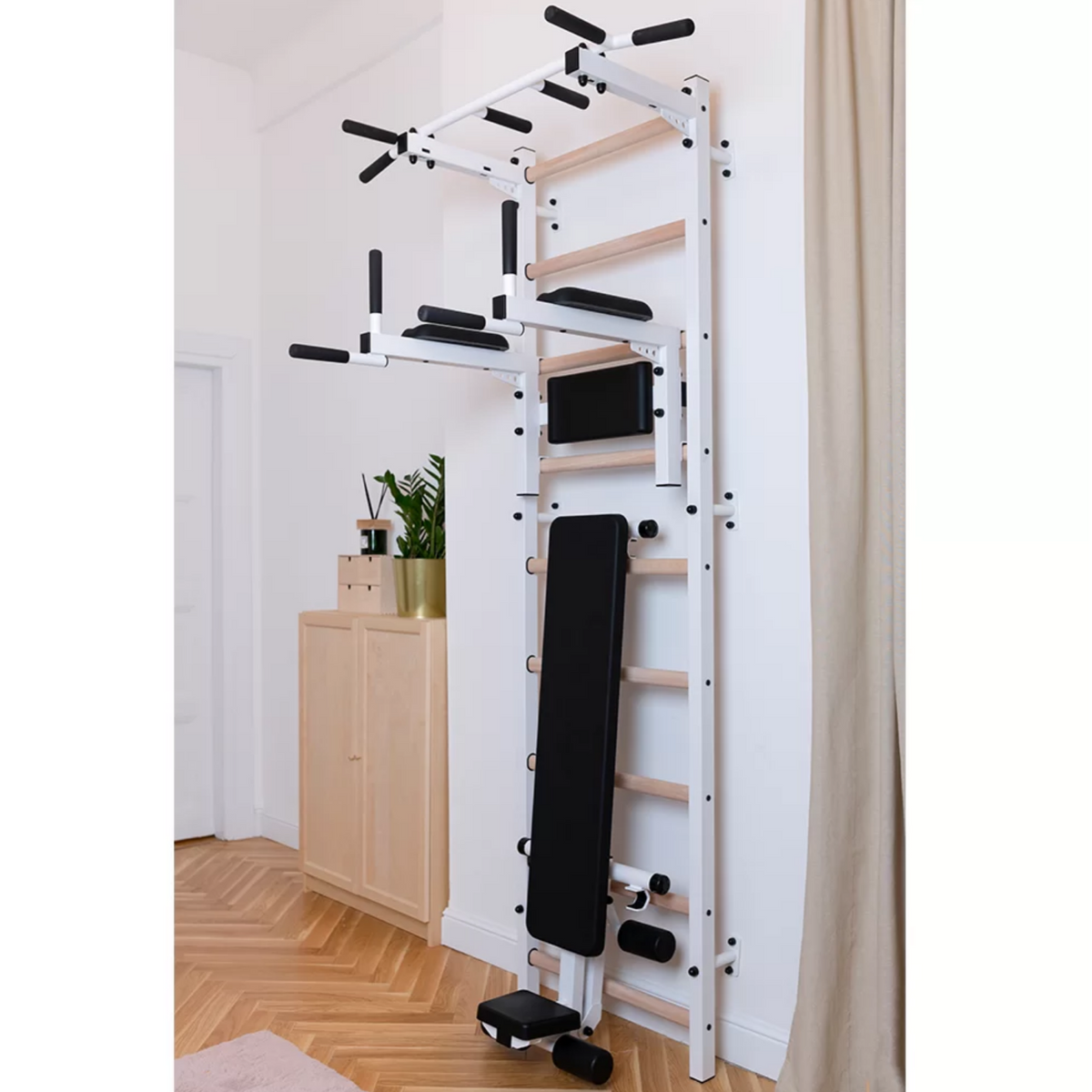 BenchK 723 Wall Bars and Gymnastic Ladders white version with pull-up bar, dip bar and workout bench installed in a bedroom.