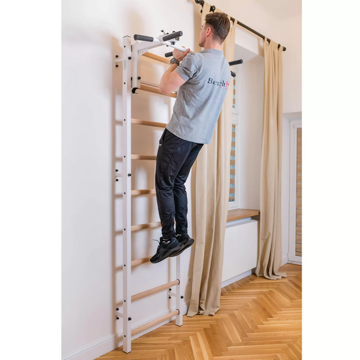 A man doing pull-ups with BenchK 731 Wall Bars and Gymnastic Ladders white version installed in a living room.