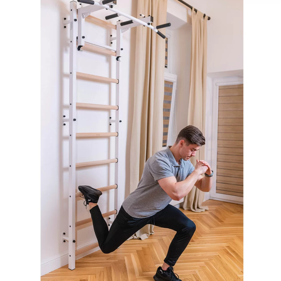 A man stretching with BenchK 731 Wall Bars and Gymnastic Ladders white version installed in a living room.