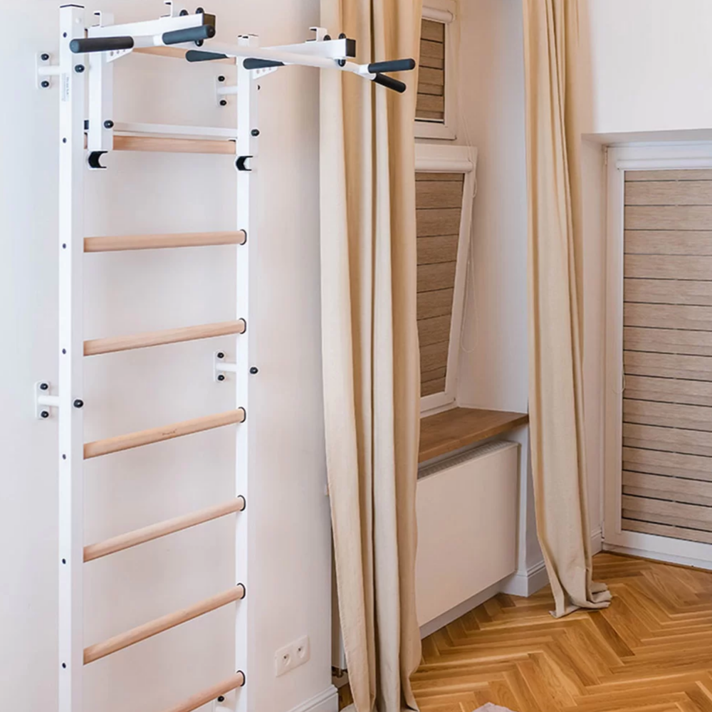 BenchK 731 Wall Bars and Gymnastic Ladders white version with pull-up bar and barbell holder installed in a bedroom.