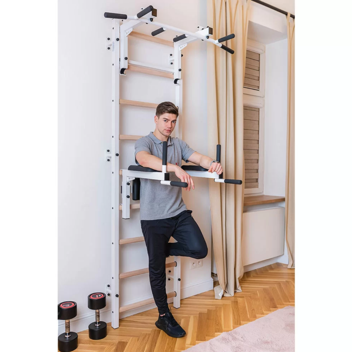 A man exercising with the BenchK 732 Wall Bars and Gymnastic Ladders white version installed in a bedroom.