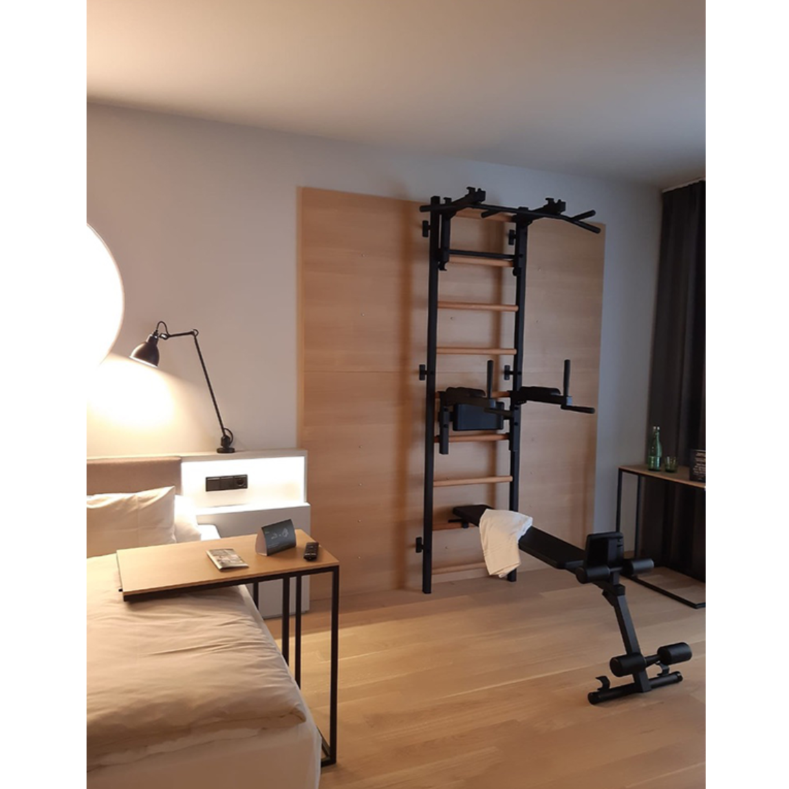 BenchK 733 Wall Bars and Gymnastic Ladders black version with pull-up bar, dip bar and workout bench installed in a bedroom.