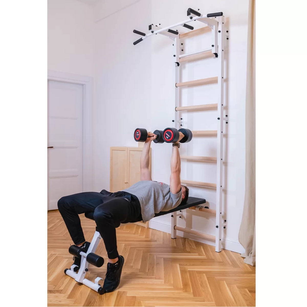 A man exercising in a BenchK 733 Wall Bars and Gymnastic Ladders white version installed in a bedroom.