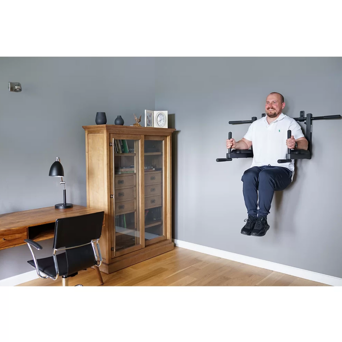 A man doing dips with BenchK D8 Pull-Up Bar and Dip Bar 2 in 1 installed in a home office.