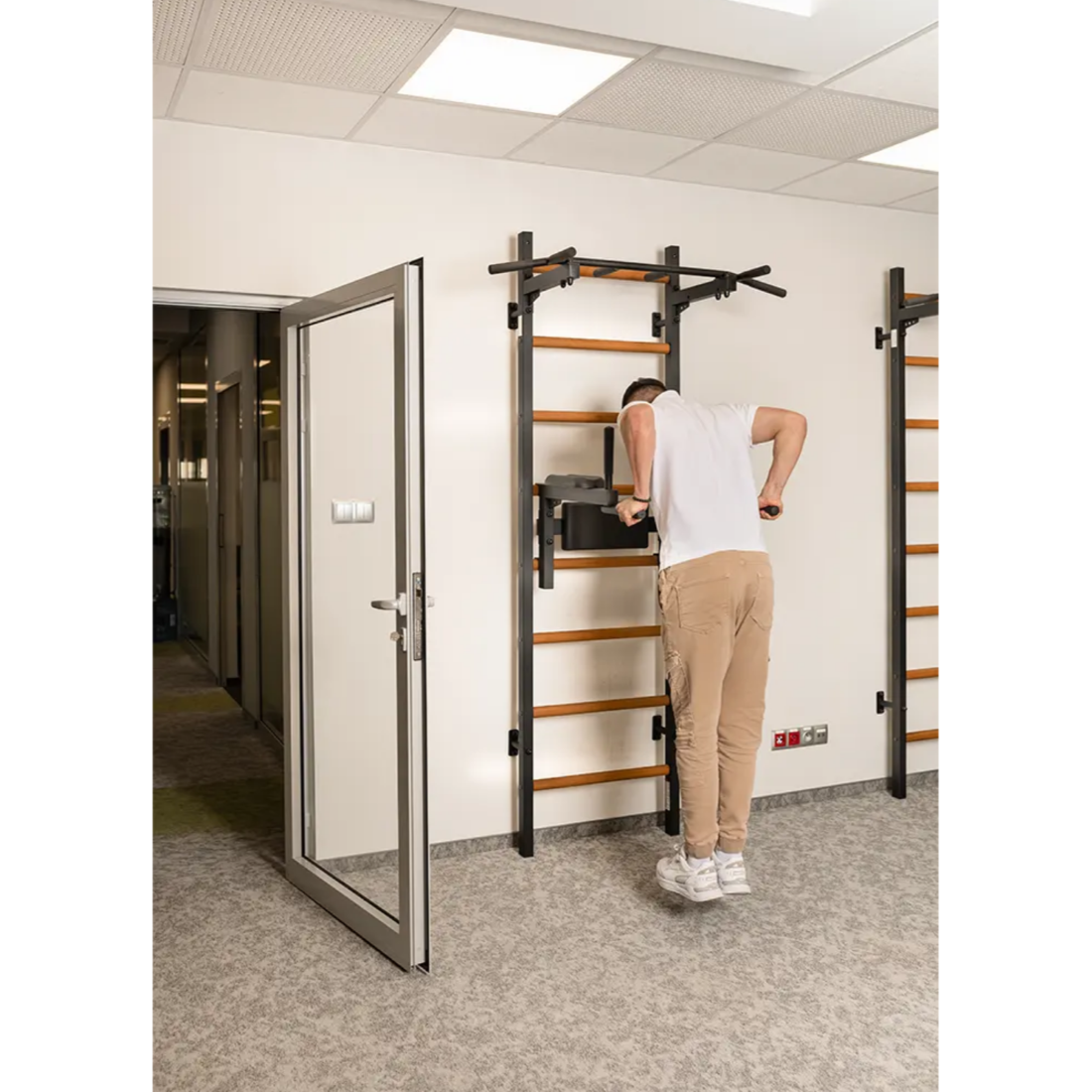 A man doing dips with BenchK DB1 Dip Bar with back support and armrest black version installed in a yoga studio.