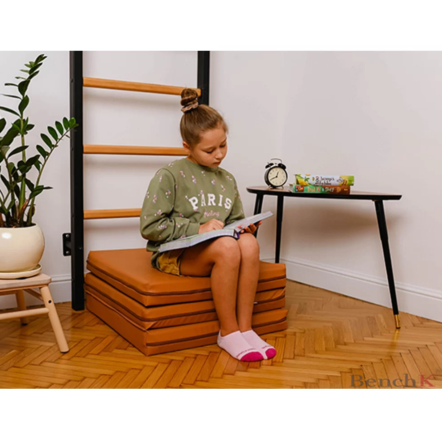 A child seated on a BenchK Foldable Gymnastic Mattress brown version.