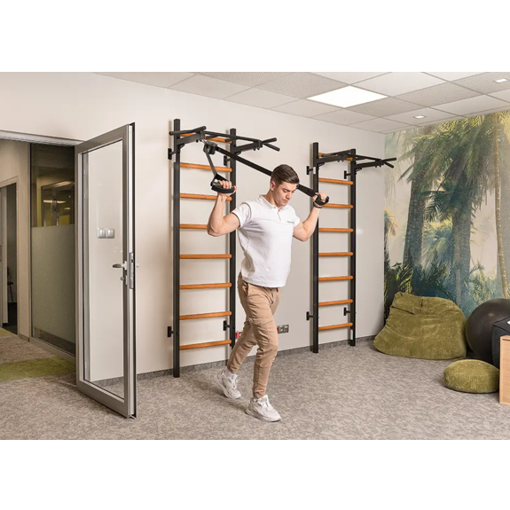 A man exercising with a TRX attached to BenchK PB2 Steel Pull-Up Bar black version installed in a gym.