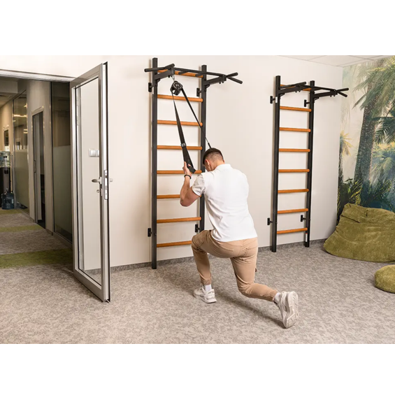 A man stretching with a TRX attached to BenchK PB2 Steel Pull-Up Bar black version.