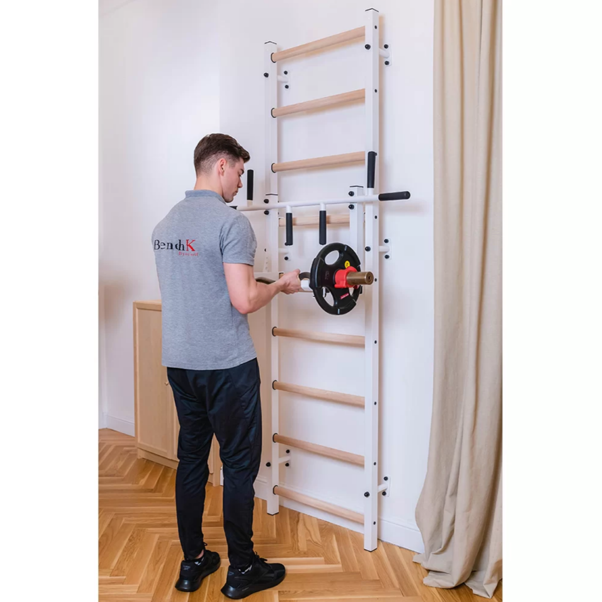 A man using BenchK PB3 Steel Pull-Up Bar with barbell holder white version installed in a bedroom.