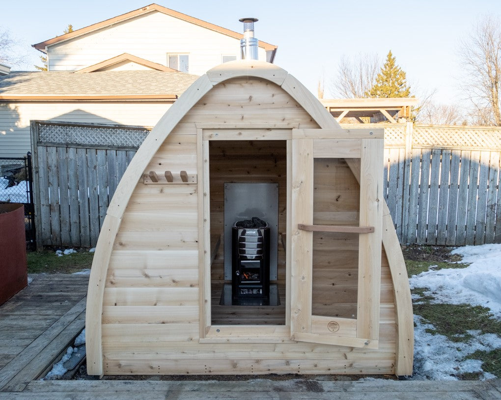 Front view of MiniPOD Outdoor Sauna with its door open in a garden. 