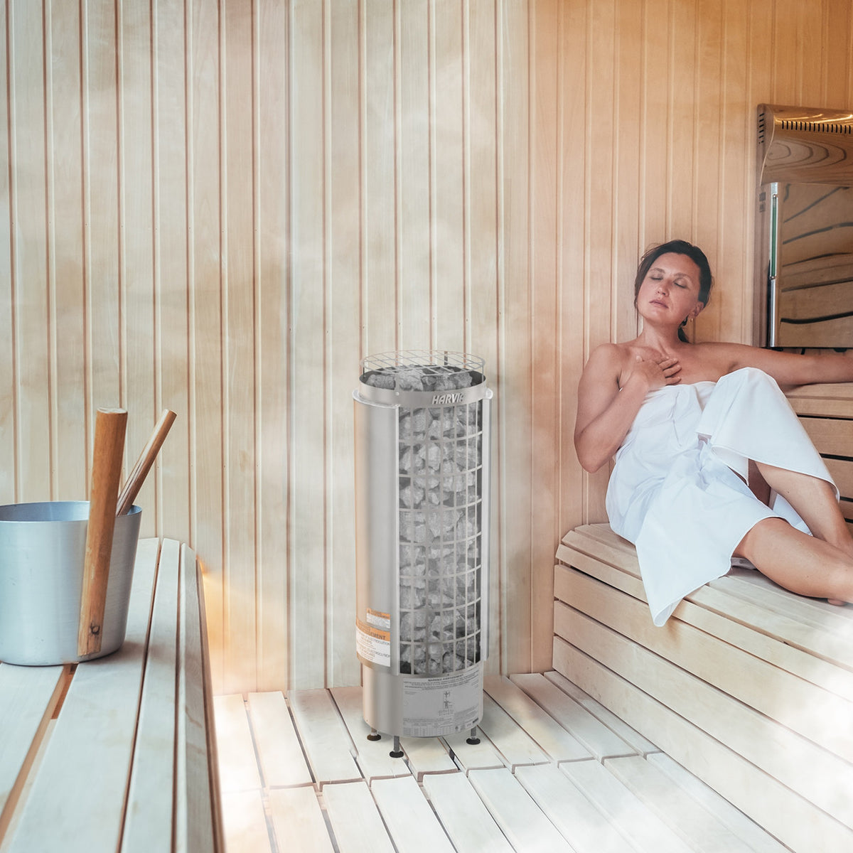 Woman relaxing in a sauna with Harvia Cilindro Electric Sauna Heater, illustrating product in use.