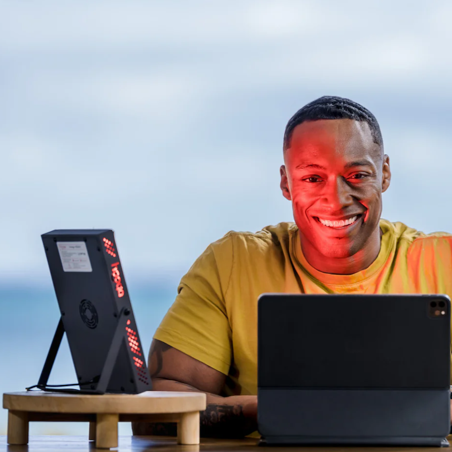 A man using a Hooga HG200 Red Light Therapy device while working at his laptop.