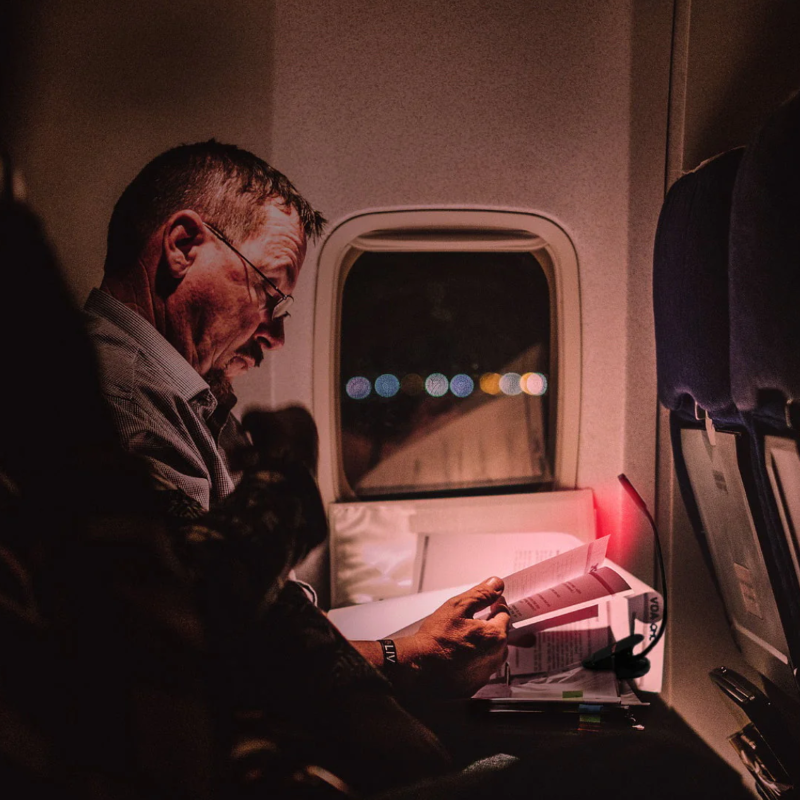 A man using a Hooga Red Clip-On Book Light during a flight at night.