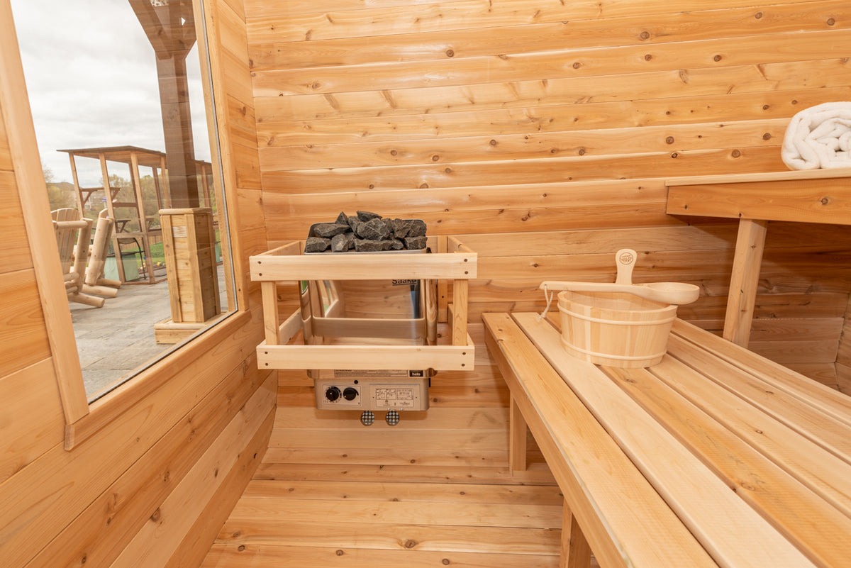 Interior view of Leisurecraft Canadian Timber Luna Outdoor Sauna, showing the door, the windows, the electric heater and the sauna bucket.