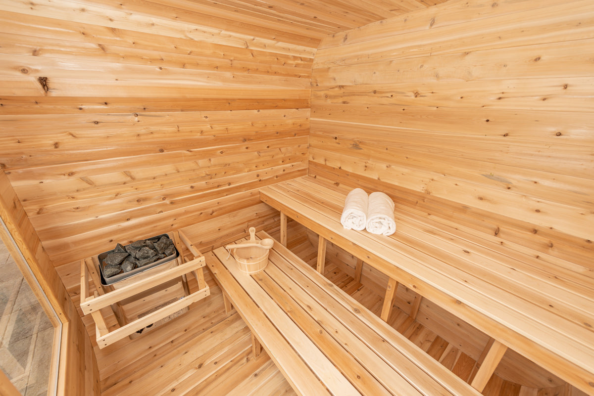 Interior view of Leisurecraft Canadian Timber Luna Outdoor Sauna, showing the benches , the electric heater and the sauna bucket.