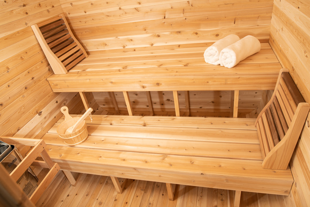 Interior view of the Interior view of Leisurecraft Canadian Timber Luna Outdoor Sauna, showing the door, the windows, the electric heater and the sauna bucket., showing the two tier benches.