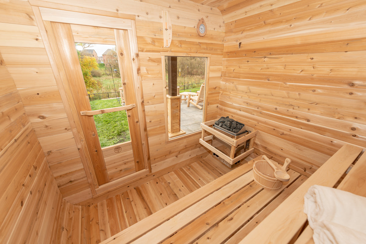 Interior view of Leisurecraft Canadian Timber Luna Outdoor Sauna, showing the door, the windows, the electric heater and the sauna bucket. 