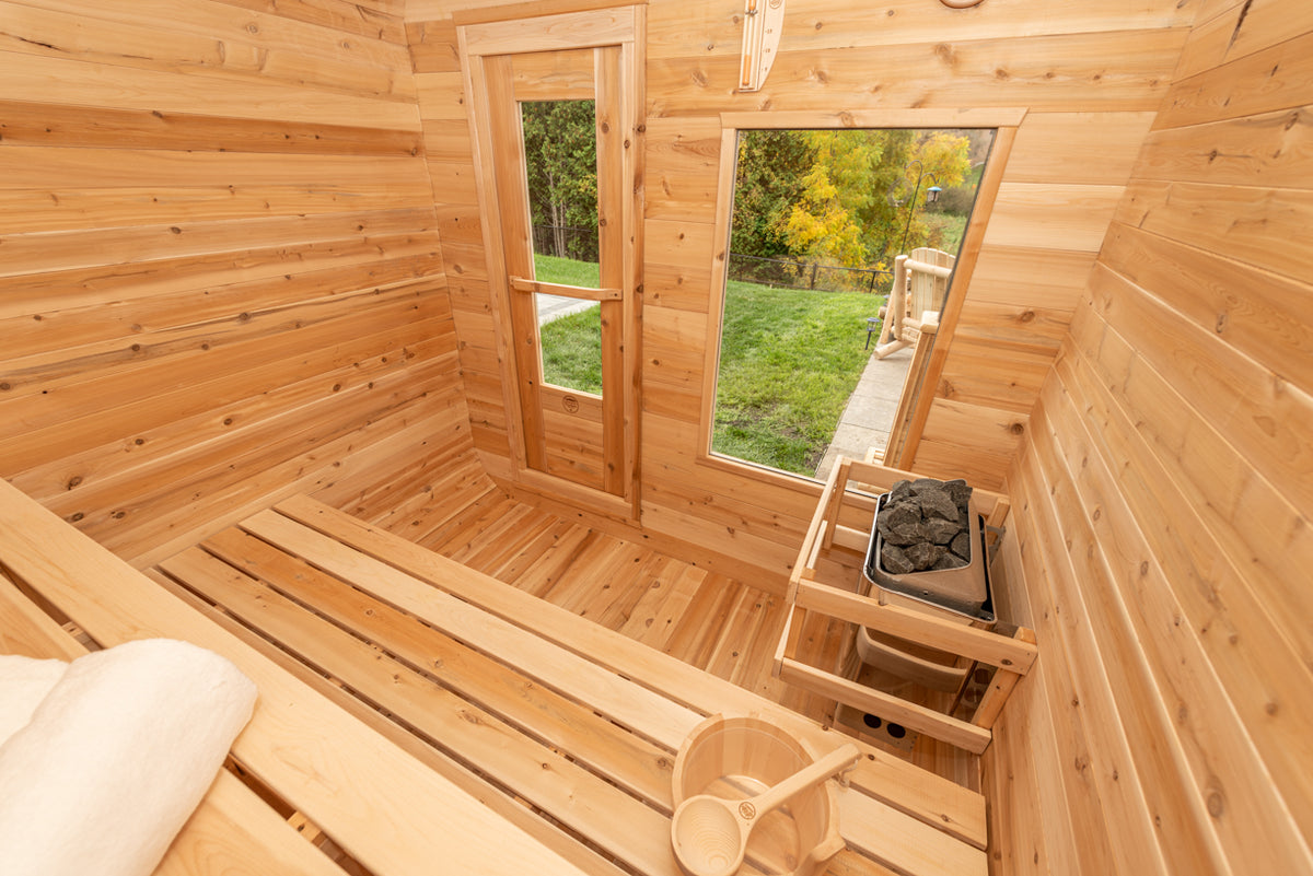 Interior view of Leisurecraft Canadian Timber Luna Outdoor Sauna, showing the door, the windows, the electric heater and the sauna bucket.