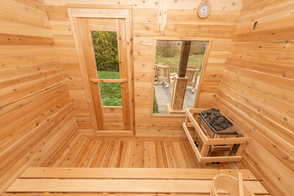 Interior view of Leisurecraft Canadian Timber Luna Outdoor Sauna, showing the door, the windows, the electric heater and the sauna bucket.