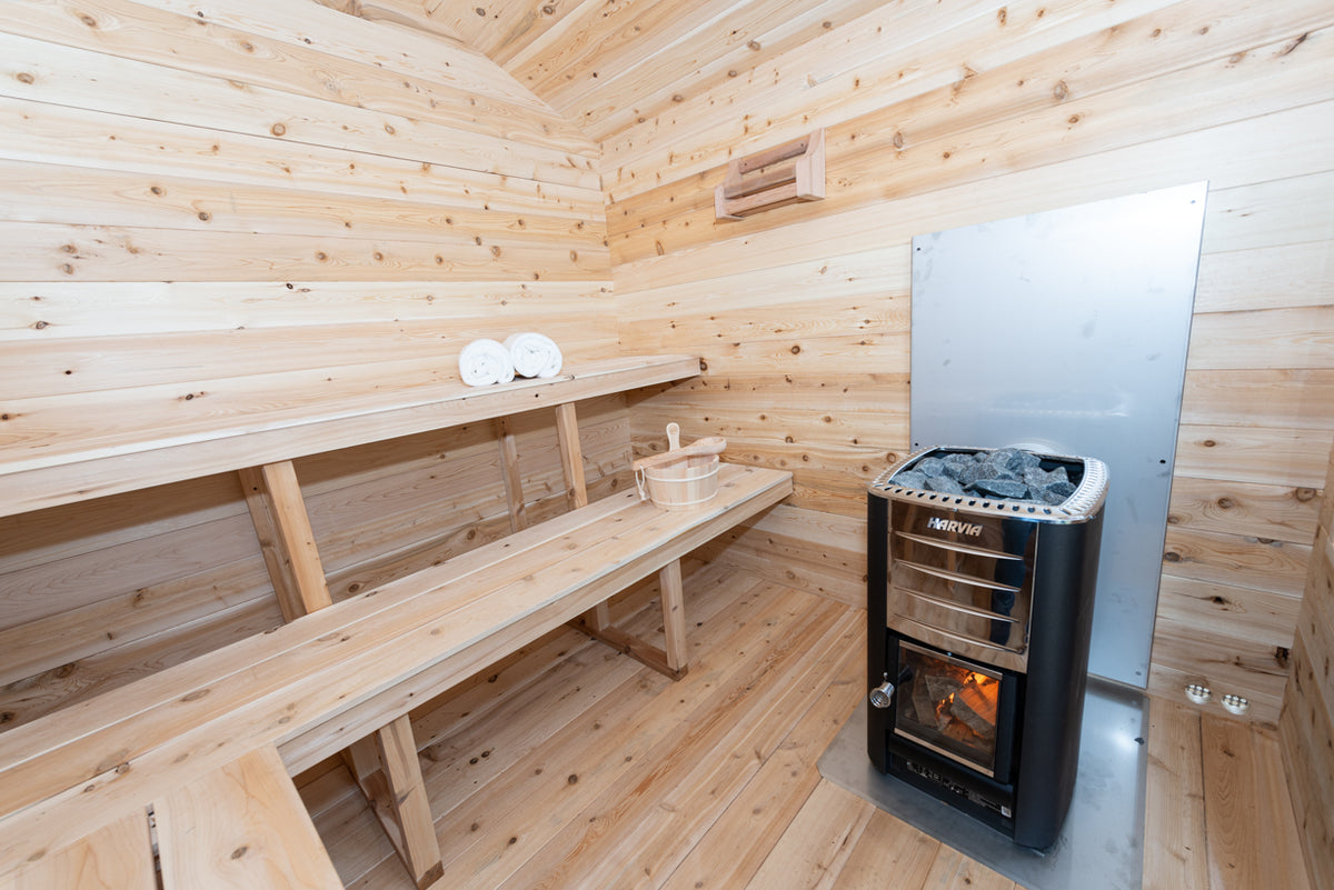 Interior view of  Leisurecraft Georgian Cabin Outdoor Sauna, with a focus on the wood burning heater and two tier benches. 