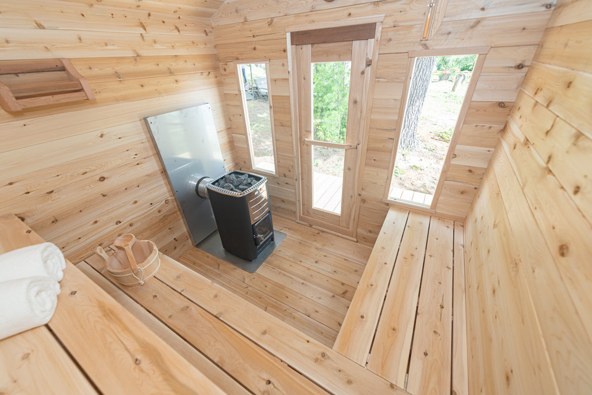 Interior view of the Georgian Cabin Outdoor Sauna, showing elements like its two tier benches, the heater, its tempered glass windows, and more.