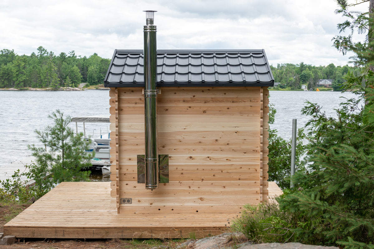 Side view of Georgian Cabin Outdoor Sauna in a natural setting with a lake in the background.