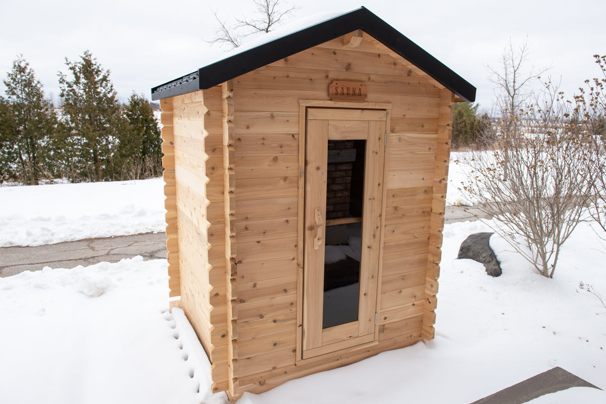 Diagonal view of Leisurecraft Canadian Timber Granby Cabin Outdoor Sauna in an outdoor setting surrounded by snow.