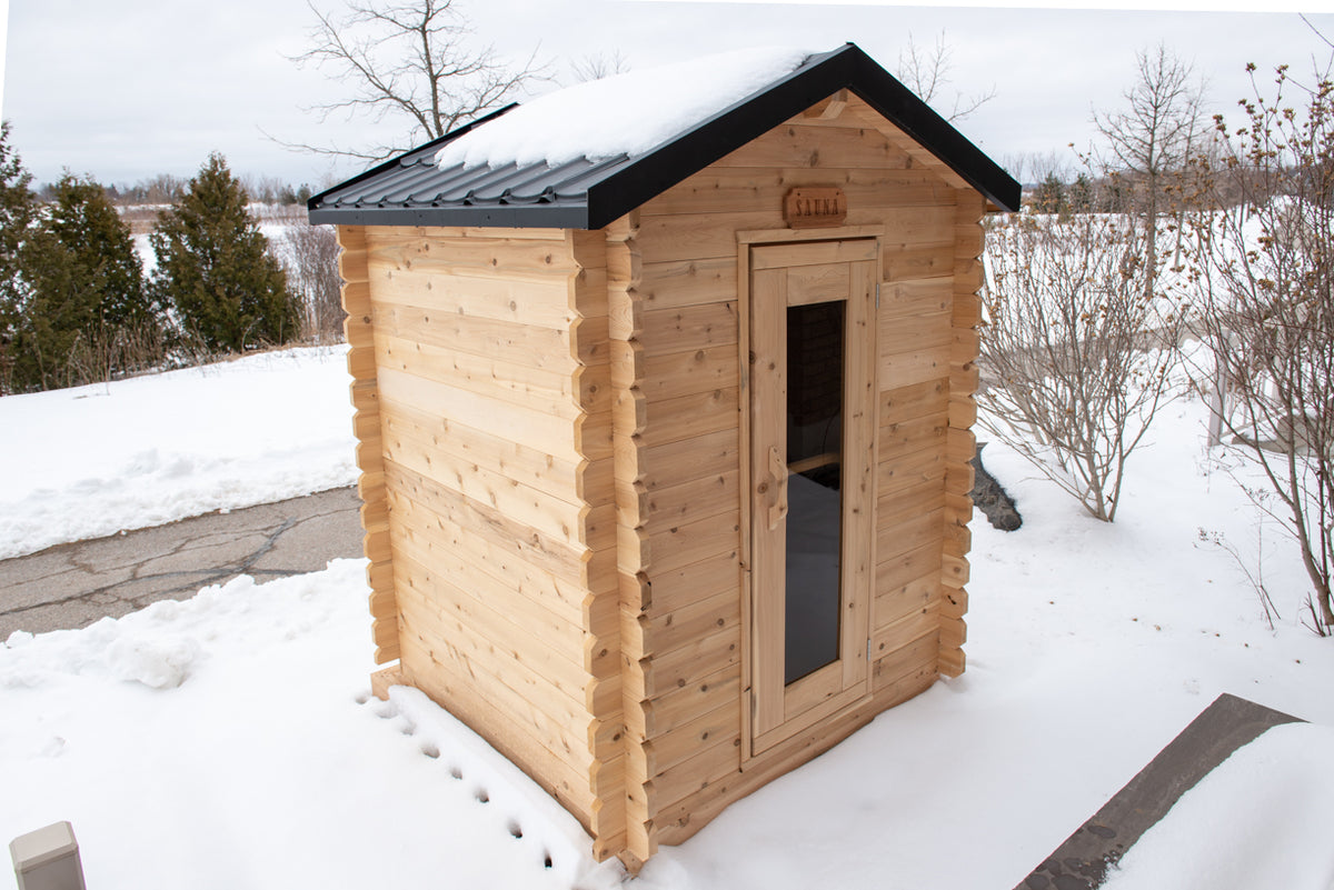 Diagonal view of Leisurecraft Canadian Timber Granby Cabin Outdoor Sauna covered by snow in an outdoor setting.