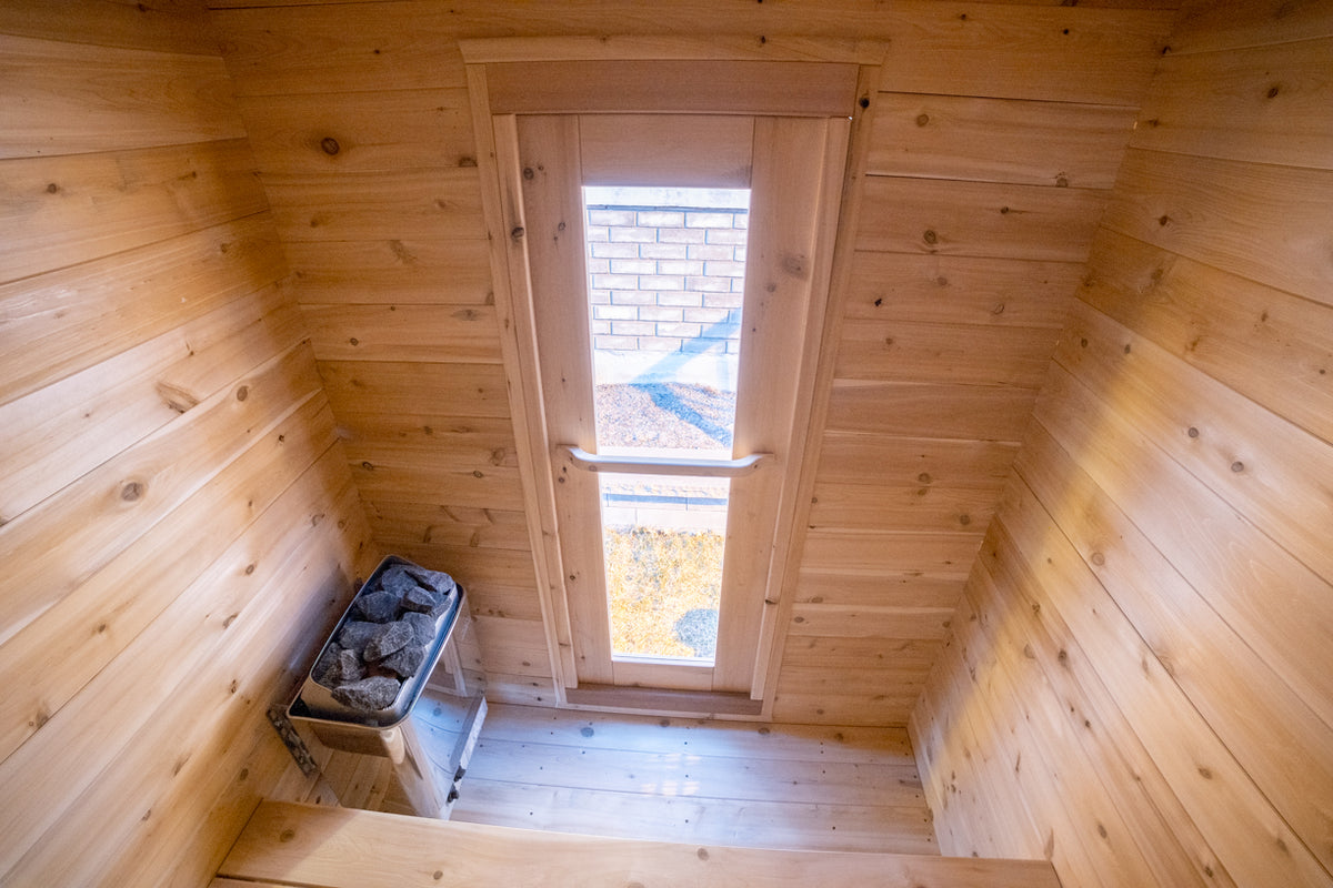 Interior view of the Leisurecraft Canadian Timber Granby Cabin Outdoor Sauna, showing the door with tempered glass and the heater. 