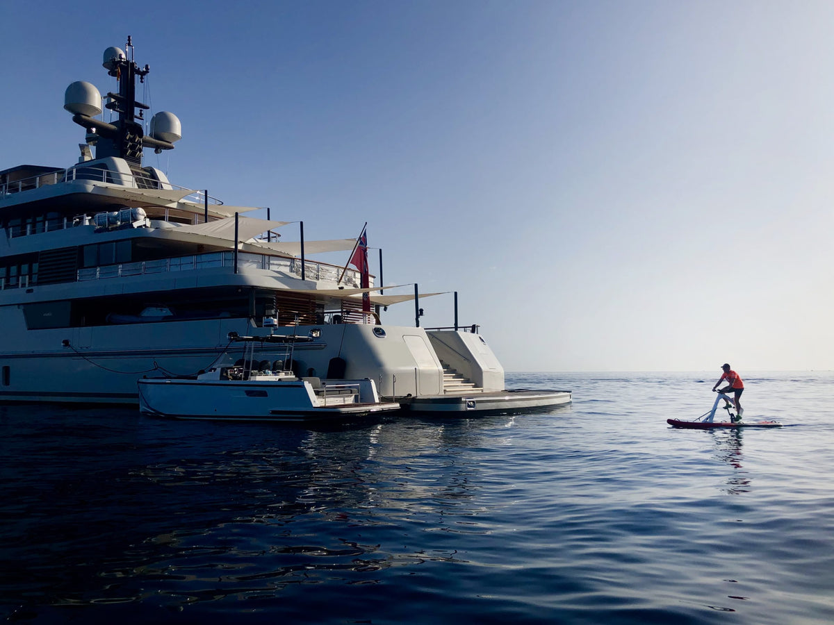 A Red Shark Enjoy Bike Surf in the foreground with a luxury yacht in the distant waters.