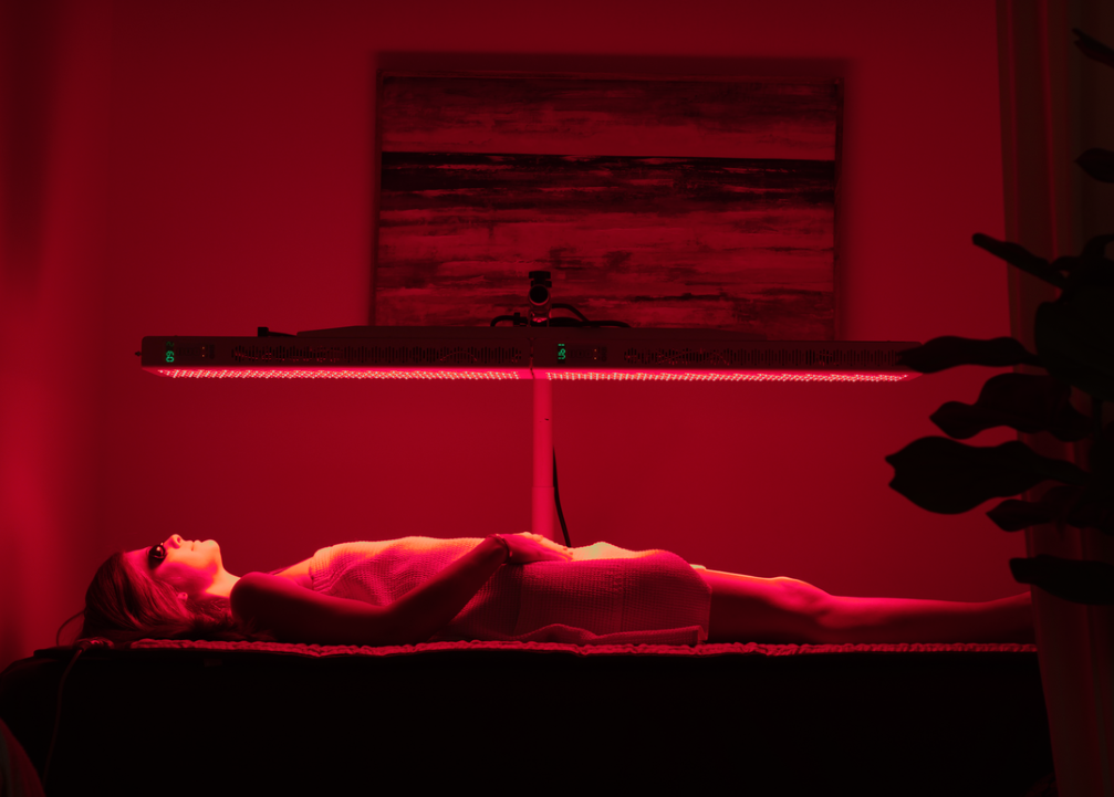 Woman relaxing under the ORB Red/NIR Light Panel during a therapeutic red light treatment session.