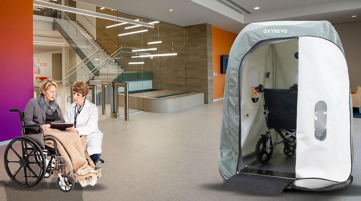 An OxyRevo Wheelchair Heal 40 1.4 ATA Hyperbaric Chamber and a patient on a wheelchair speaking with her doctor in an indoor setting.