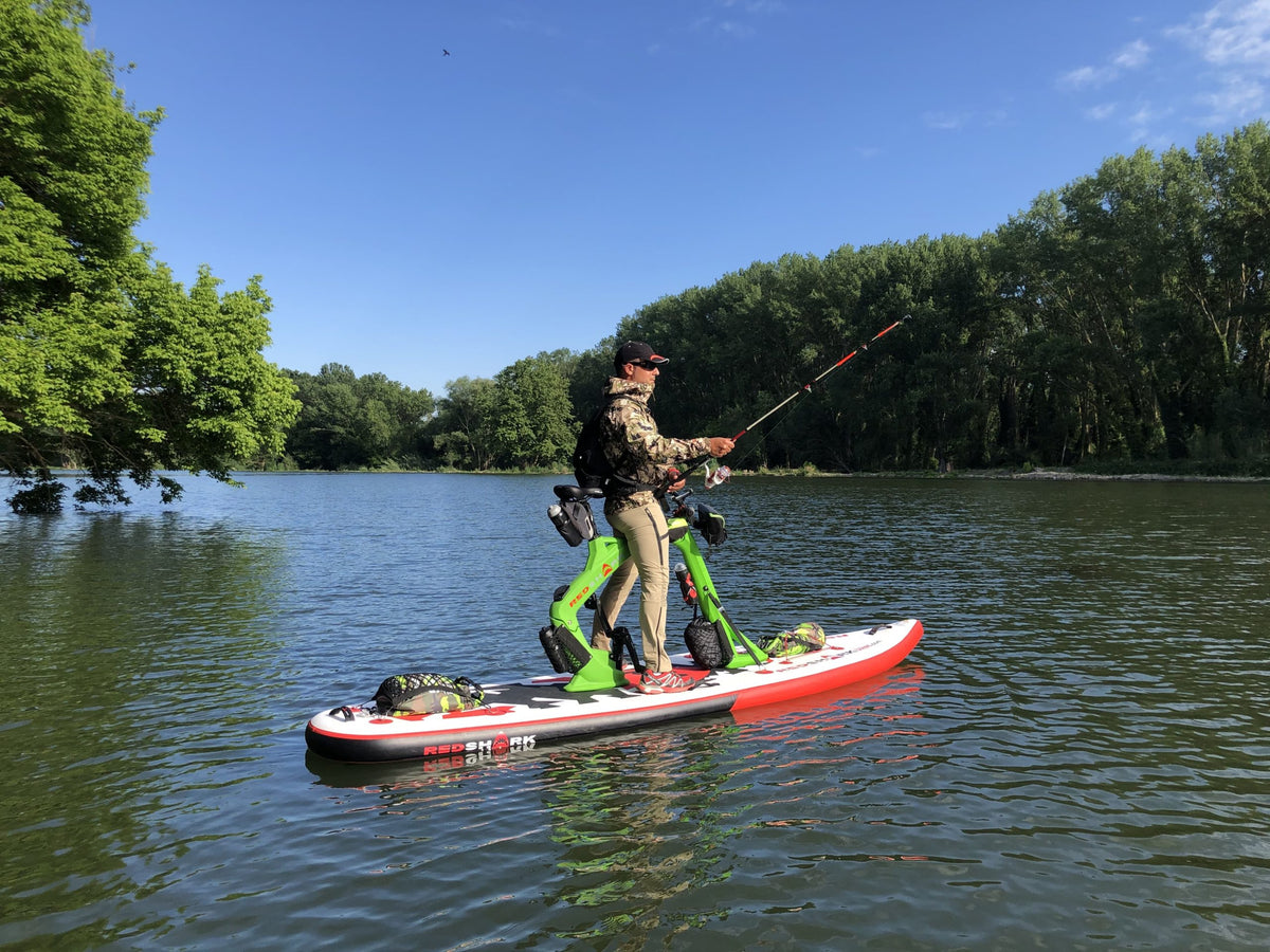 Outdoor enthusiast fishing on a Red Shark Adventure Bike Surf against a backdrop of lush greenery.