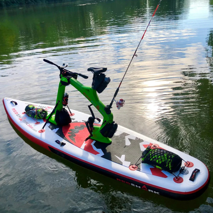 Inflatable Red Shark Adventure Bike Surf equipped with fishing gear floating near shore.