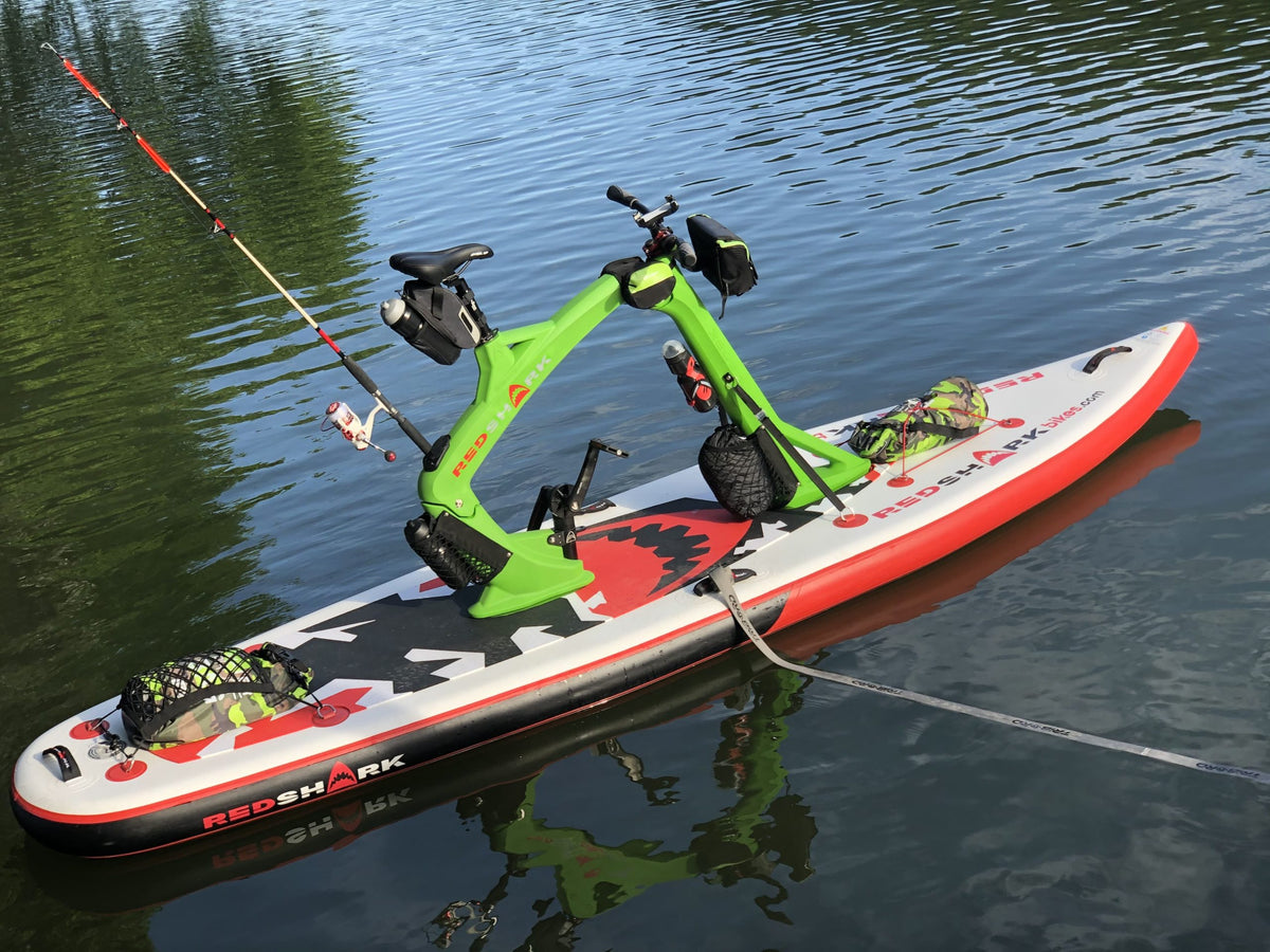 Inflatable Red Shark Adventure Bike Surf equipped with fishing gear floating near shore.