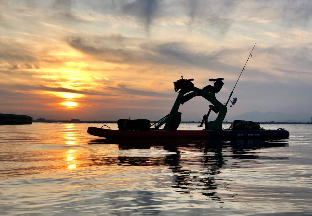 Silhouette of Red Shark Adventure Bike Surf against a stunning sunset over the water.