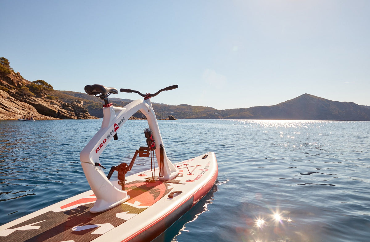 A tranquil Red Shark Enjoy Bike Surf experience by the seaside with mountain landscape in the backdrop.