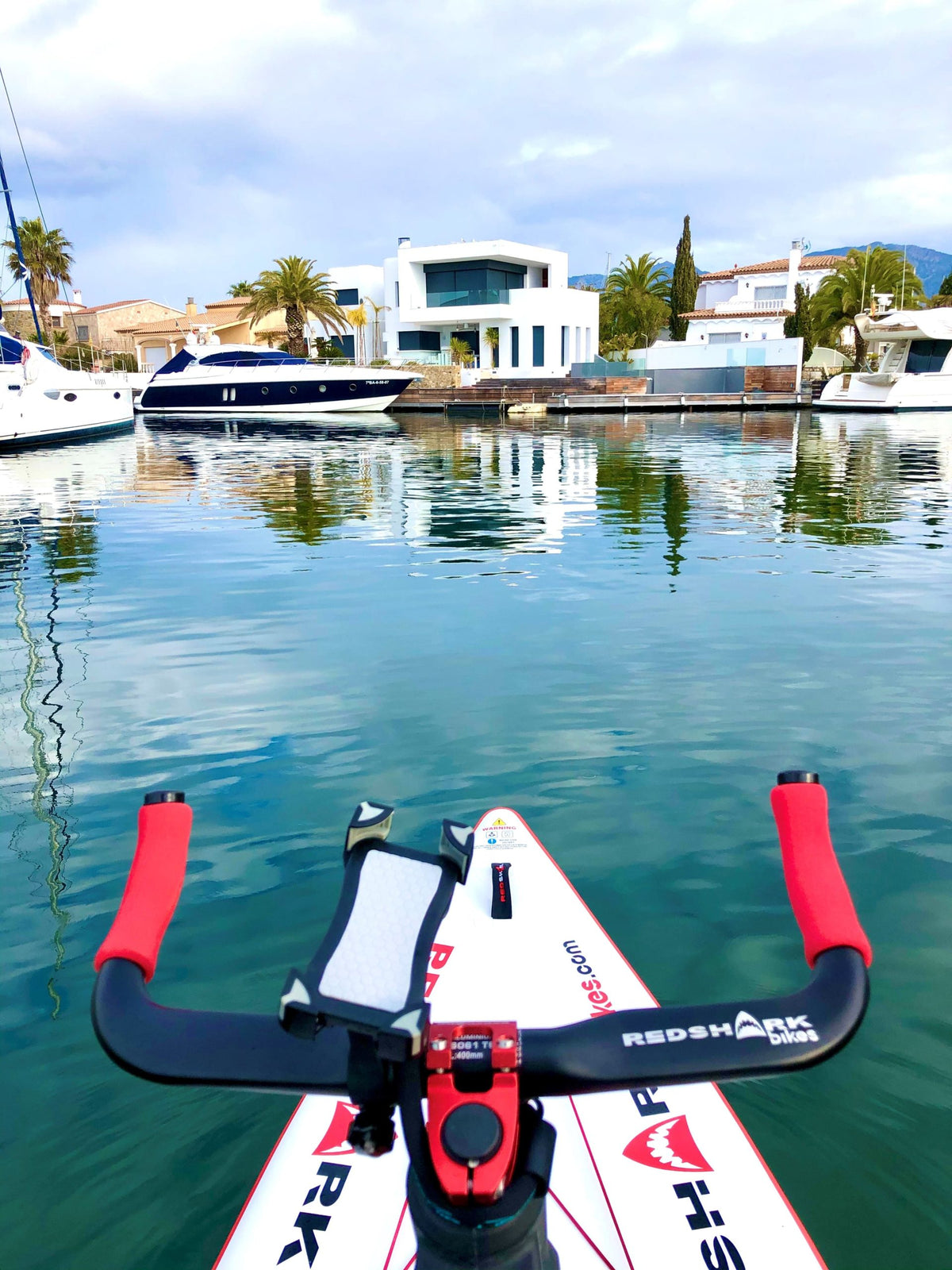 Red Shark Fitness Bike Surf docked at a marina with luxury boats in the background.