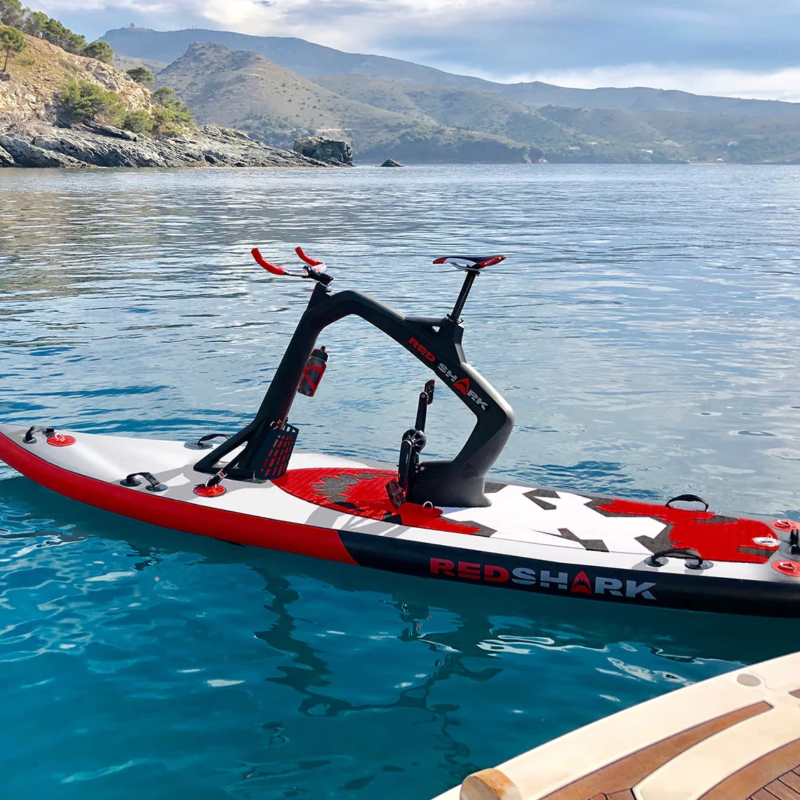 Red Shark Fitness Bike Surf floating near a mountainous coastline on a clear day.